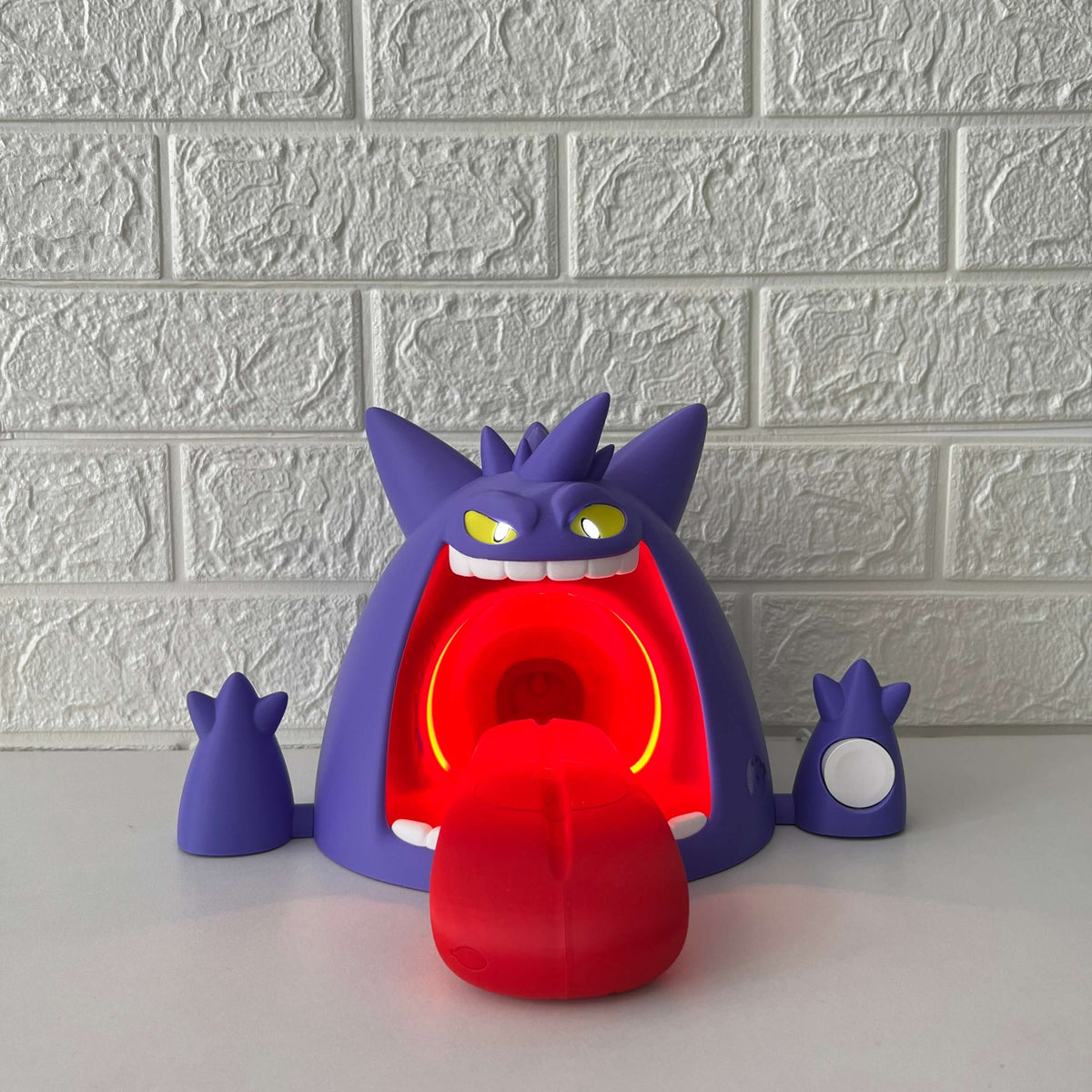 Gengar-inspired wireless charging stand with red LED lighting on, front view on desk background