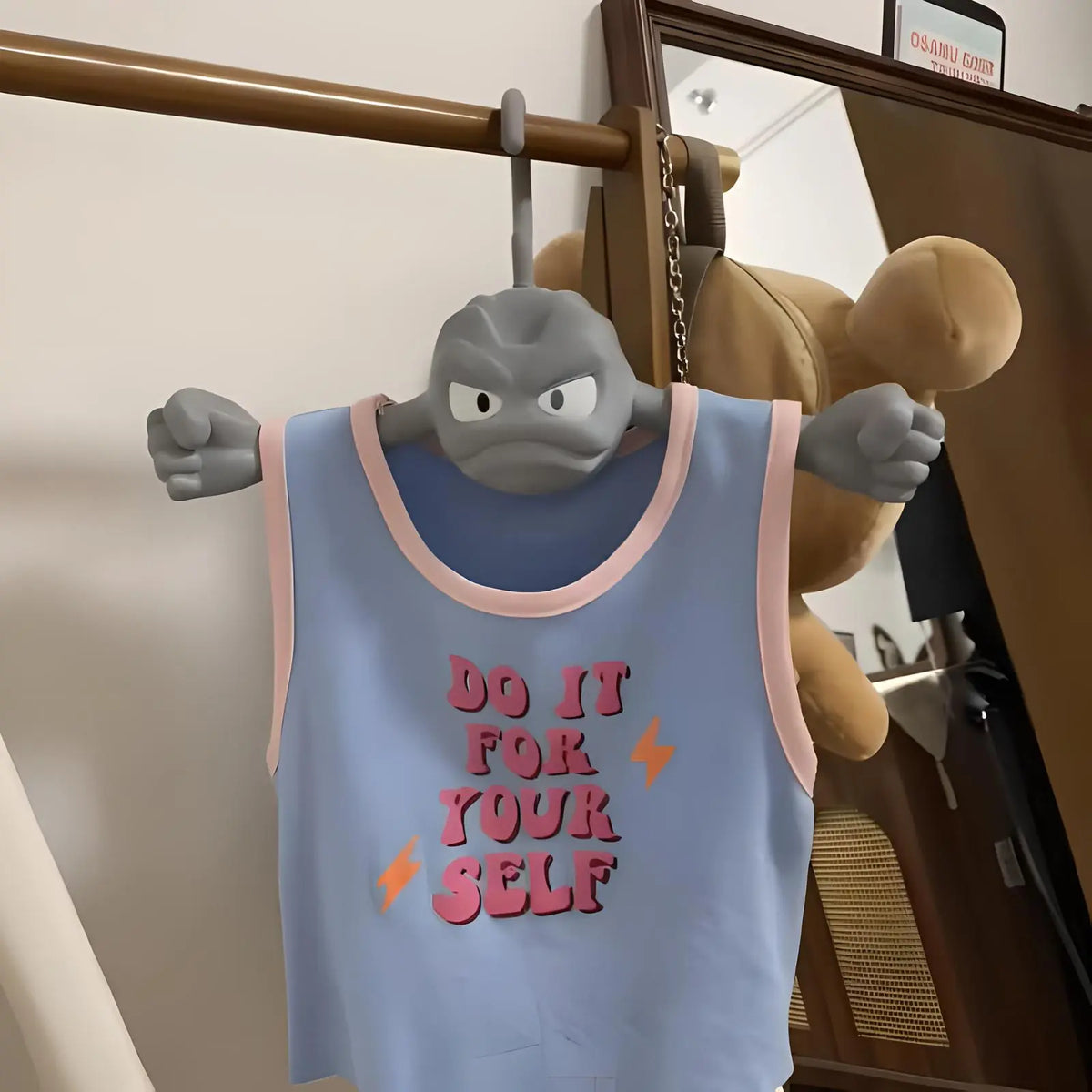A novelty Geodude coat hanger holding a light blue tank top that reads Do It For Yourself.