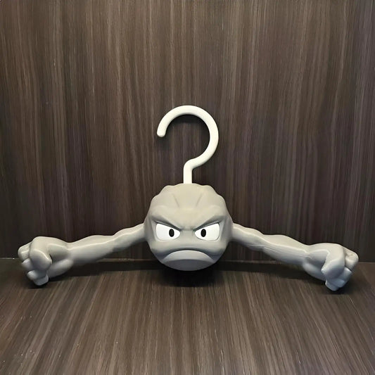 Anime-inspired Geodude clothes hanger with flexing rock arms against a dark wood wall background.